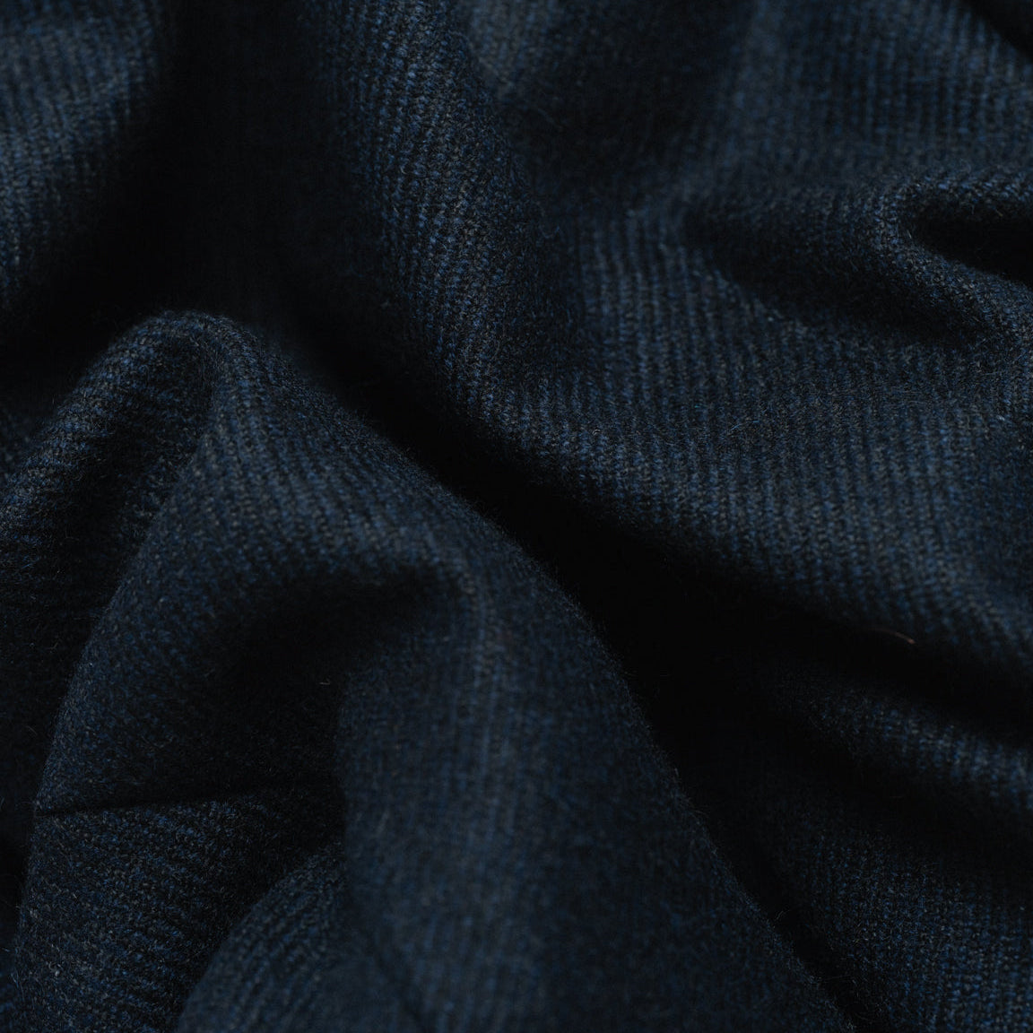A close-up of dark navy blue ribbed fabric with soft folds and a fine knit texture.