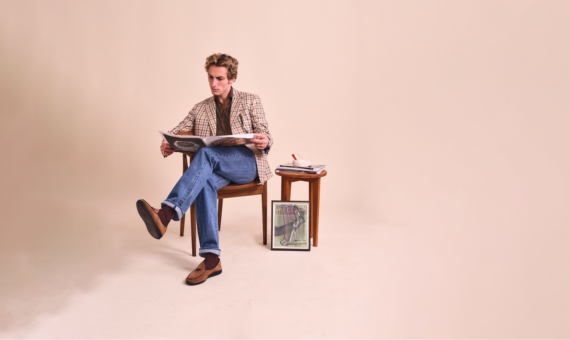 Man sitting on a chair reading a book with a small table beside him on a beige background